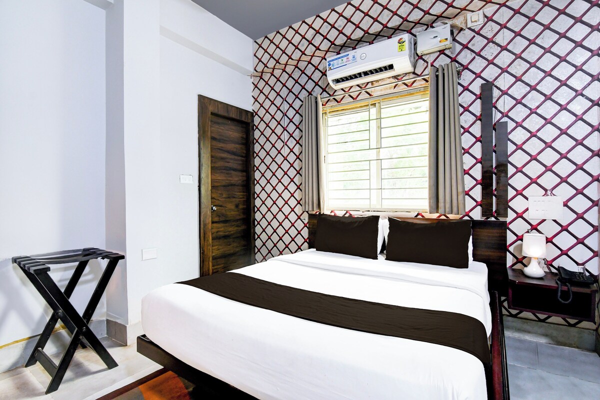 Habitación de hotel con cama, ventana con vistas, aire acondicionado, mesita de noche con lámpara y teléfono.