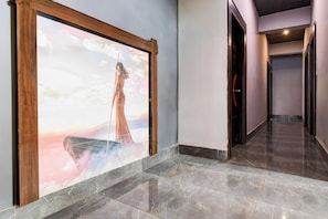 Un pasillo con una obra de arte grande enmarcada a la izquierda, una puerta con picaporte rojo a la derecha y un piso de baldosas.