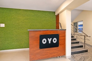 Un mostrador de recepción con un letrero que dice 'OYO' en un edificio moderno con una pared verde y una escalera.