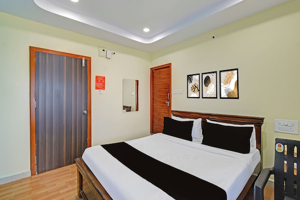 Habitación de hotel con una cama, una puerta de madera, un espejo y dos cuadros en la pared.