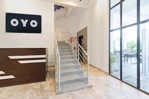 A reception area with a staircase leading to an upper floor, a large window offering a view of the outdoors, and a sign with the word 'OYO' on the wall. - Hotel O Zest Inn (Hyderabad)