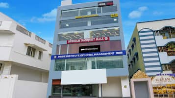A multi-story building with signage for 'PRIDE Rooms,' 'SUBHAM BANQUET HALL,' and 'PRIDE INSTITUTE OF HOTEL MANAGEMENT.'