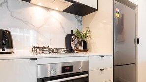 Sleek kitchen workspace equipped with a built-in gas cooktop, oven, dark fixtures, and marble-style splashback tiling.    - Richmond Rhythm | City Living & Lifestyle (Richmond)