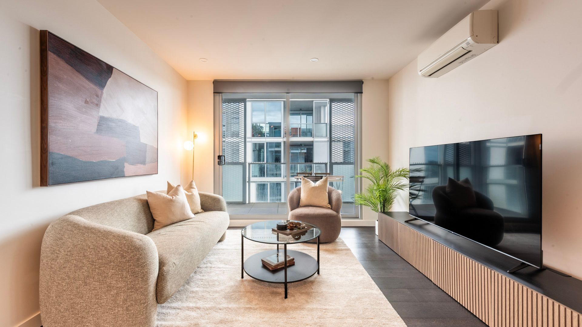 Een moderne woonkamer met een bank, fauteuil, salontafel, televisie en kunstwerk.