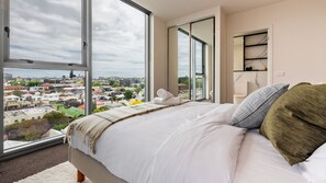 A bedroom with a large window, a bed, and a view of a cityscape. - Richmond Rhythm | City Living & Lifestyle (Richmond)