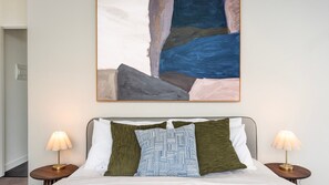 A hotel room with a bed, two bedside lamps, and a large abstract painting above the bed. - Richmond Rhythm | City Living & Lifestyle (Richmond)