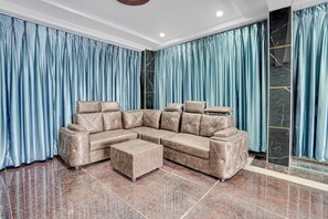 Sala moderna com sofá seccional, um banquinho e piso de mármore.