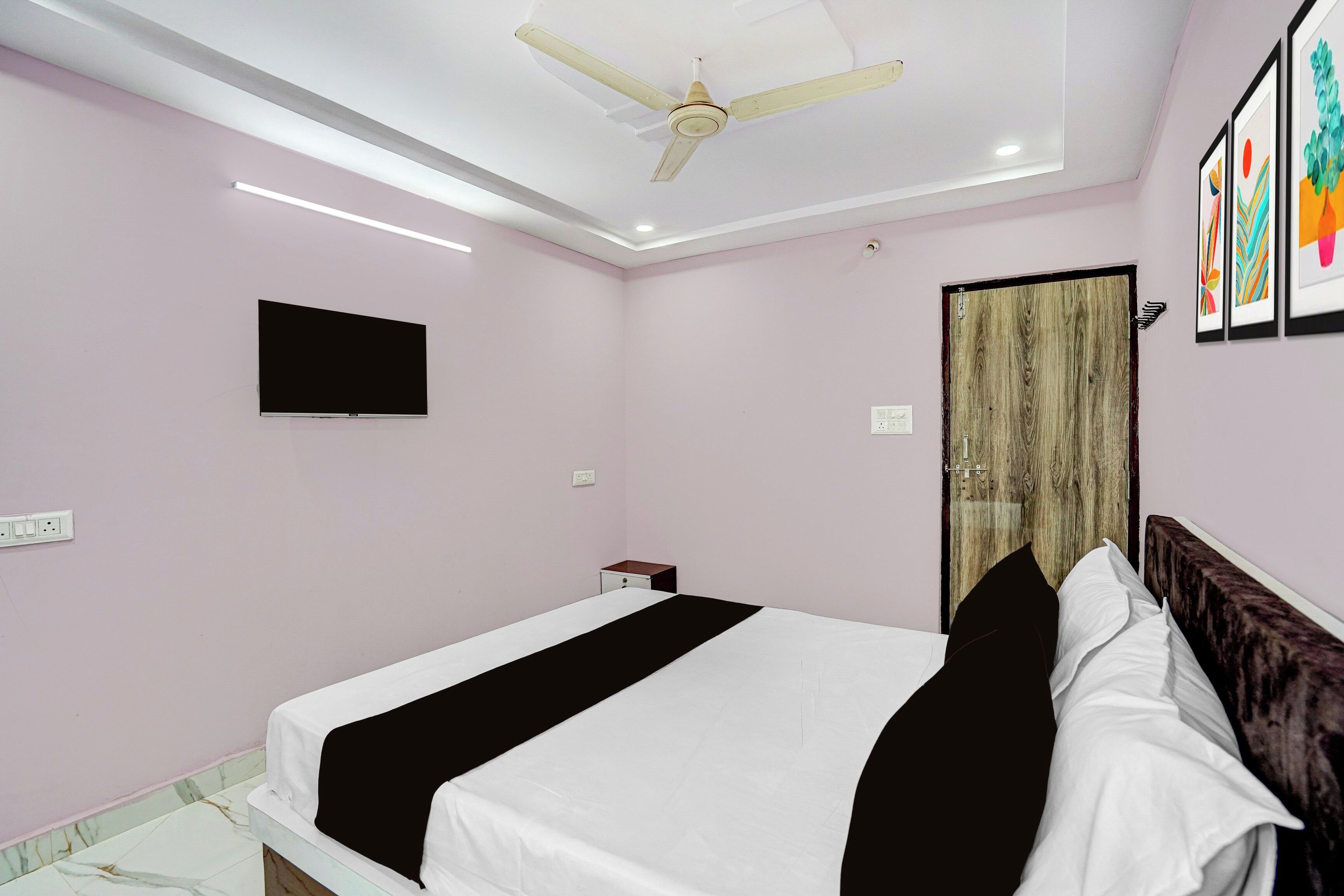 Habitación de hotel con cama, ventilador de techo, televisor de pantalla plana y una obra de arte en la pared.