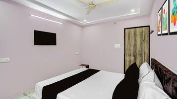 Habitación de hotel con cama, ventilador de techo, televisor de pantalla plana y una obra de arte en la pared.