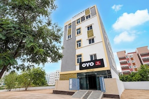 Un moderno edificio de hotel con un cartel llamativo que muestra 'OYO VSK Grand Stay' y 'V8 Heights' en la fachada.