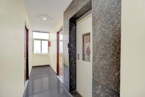 A hallway with a marble wall, a door with a poster, and a window with a view of buildings.