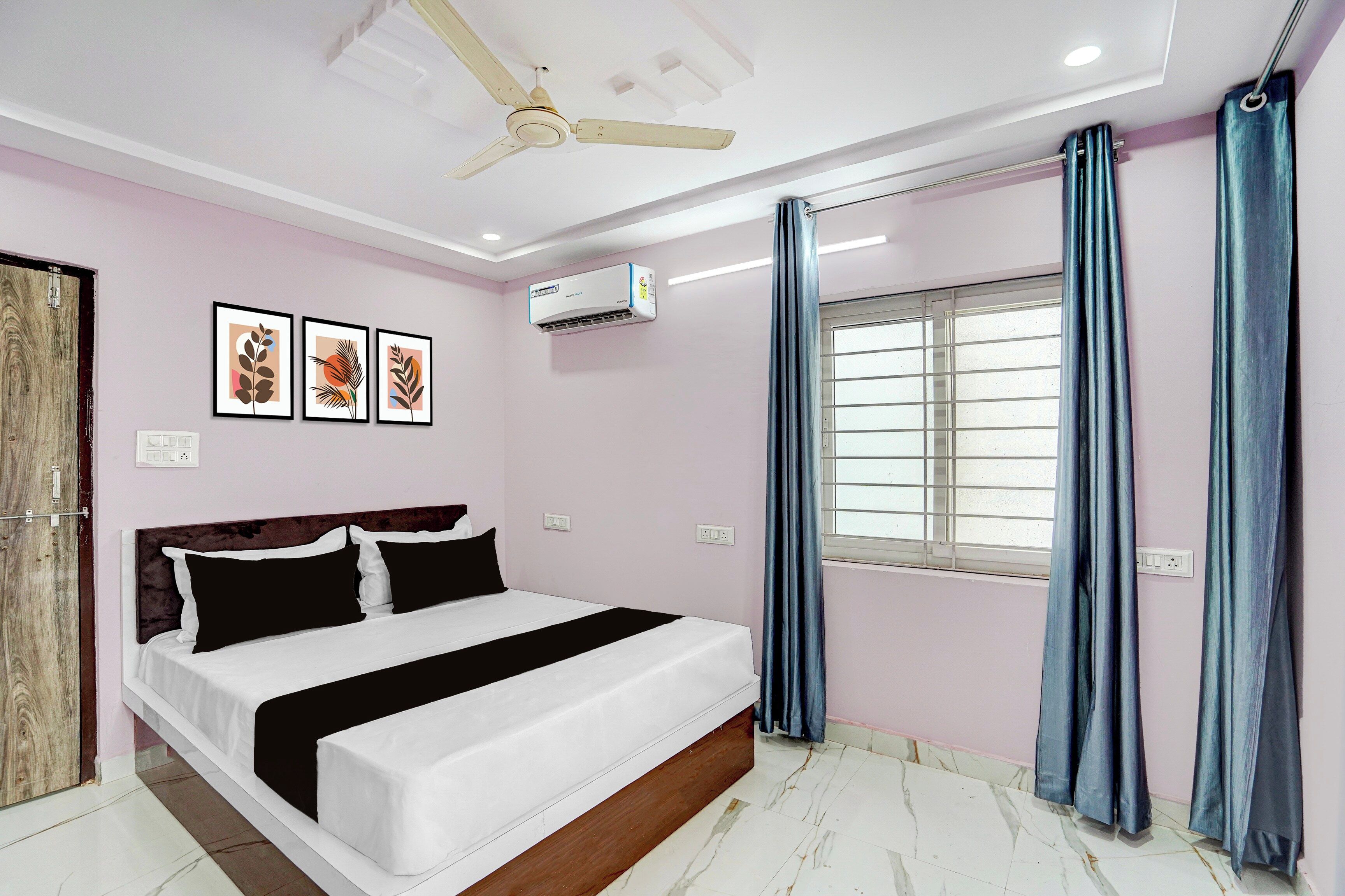 A bedroom with a bed, a ceiling fan, an air conditioning unit, a window with curtains, and framed artwork on the wall.