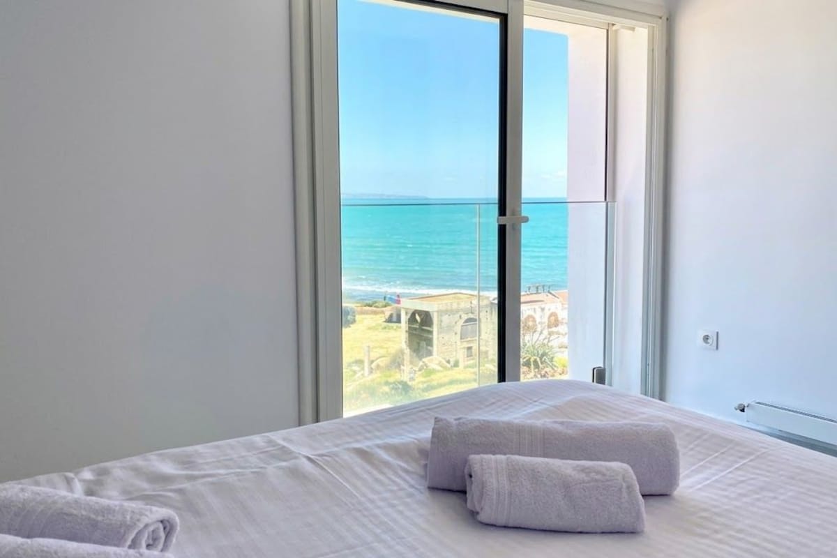 Ein Schlafzimmer mit großem Fenster und Blick auf die Küste.