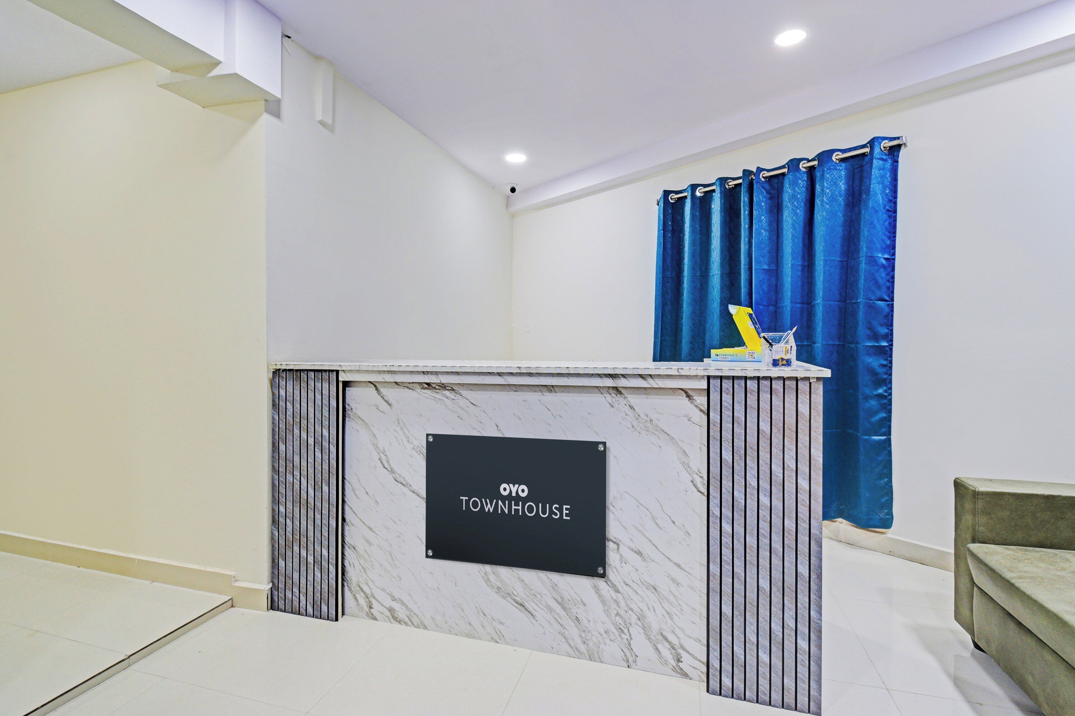 A reception desk with a sign reading 'OYO TOWNHOUSE' in a modern interior with white walls and a blue curtain.
