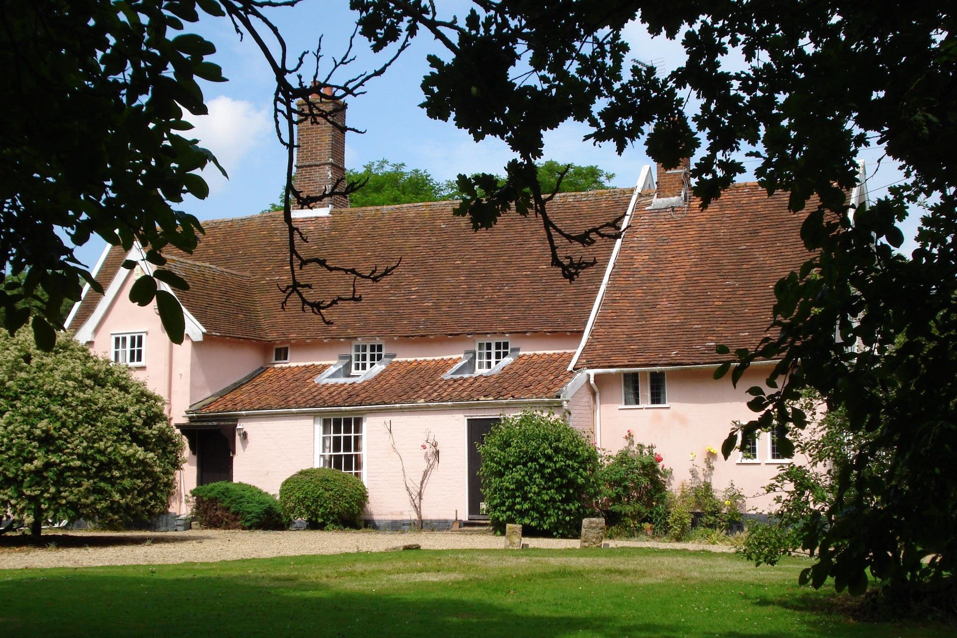 Une maison à deux étages, dotée d’un toit à deux versants, d’une cheminée en briques et d’un jardin bien entretenu.