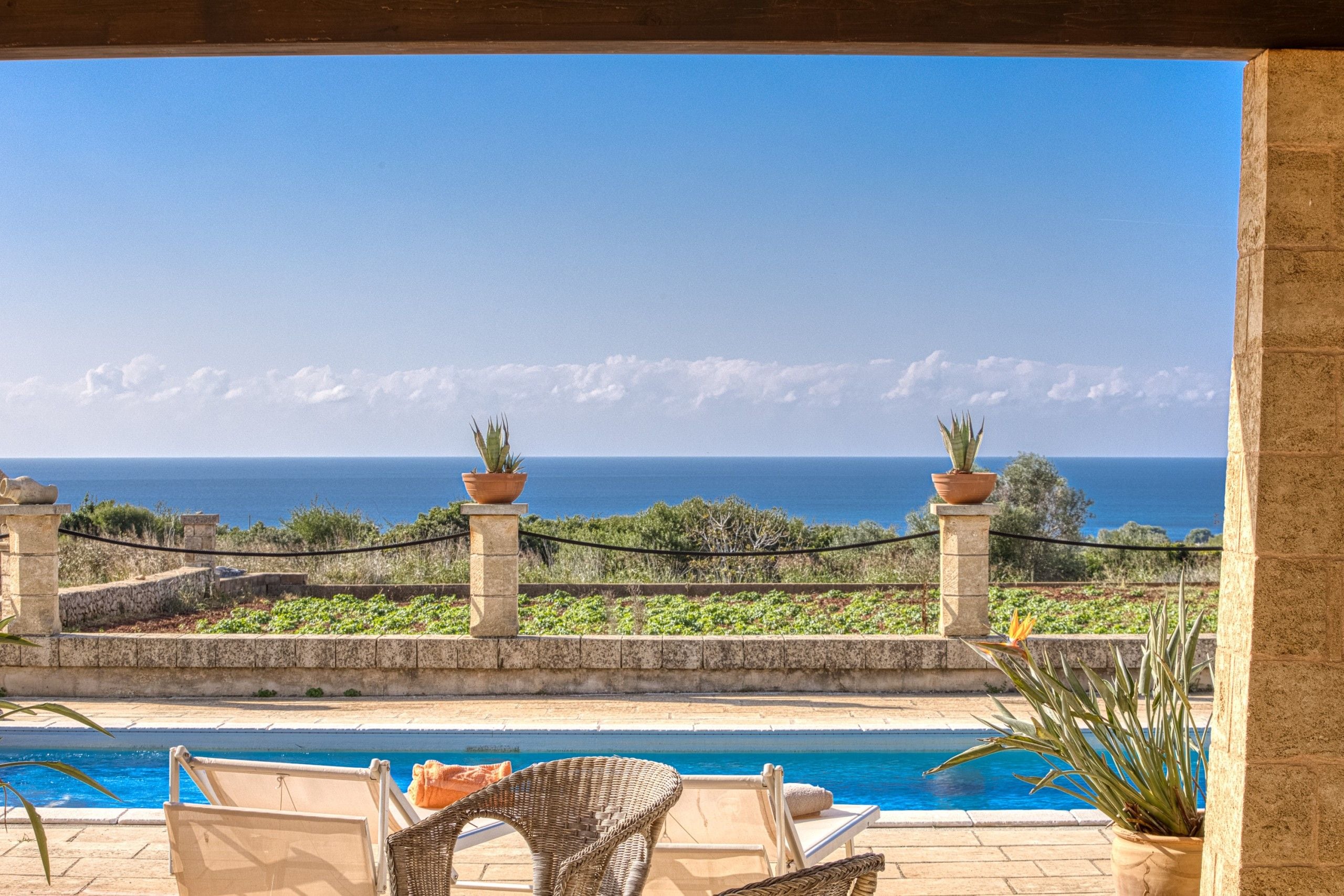 A pool area with lounge chairs and a view of the sea.