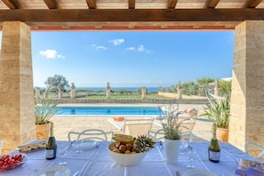 A dining area with a view of a pool and the sea, featuring a table set with wine glasses, a bowl of fruit, and bread. - Villa 'Kambusa Homes -  Lido Marini' with Sea View, Wi-Fi and Air Conditioning (Salve)