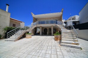 A building with a central courtyard, a staircase leading to a balcony, and a clear blue sky. - Apartment 'Kambusa Homes - Al Porto - Destra' with Sea View, Wi-Fi and Air Conditioning (Torre Vado)