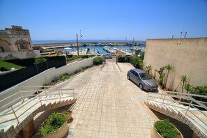 A paved pathway leading to a marina with boats, a parked car, and a castle-like structure. - Apartment 'Kambusa Homes - Al Porto - Destra' with Sea View, Wi-Fi and Air Conditioning (Torre Vado)