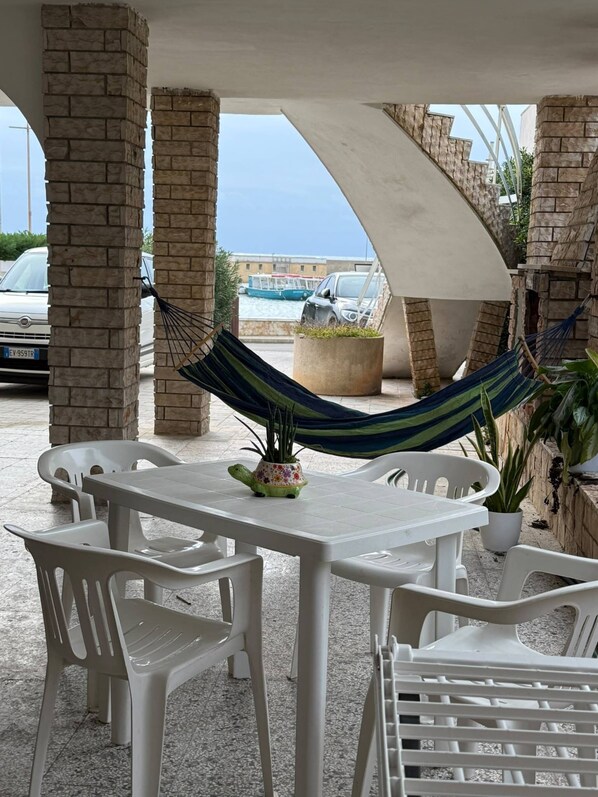 An outdoor patio with a table and chairs, a hammock, and a view of the sea. - Apartment 'Kambusa Homes - Al Porto - Sinistra' with Sea View, Wi-Fi and Air Conditioning (Torre Vado)