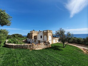 A historic building with a stone facade, arched windows, and a balcony overlooking a grassy area with a clear view of the sea. - Apartment 'Kambusa - Pozzo Pasulo - A' with Sea View, Wi-Fi and Air Conditioning (Morciano di Leuca)