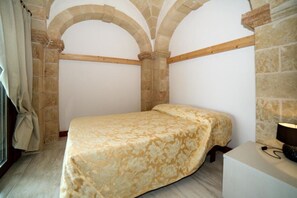A bedroom with a bed, a nightstand, and stone walls. - Apartment 'Kambusa - Pozzo Pasulo - A' with Sea View, Wi-Fi and Air Conditioning (Morciano di Leuca)