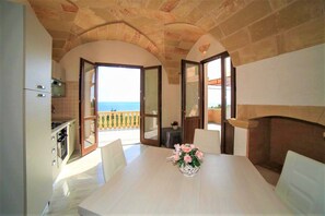 A dining area with a table, chairs, a vase with flowers, a fireplace, and an open door leading to a balcony with a view. - Apartment 'Kambusa - Pozzo Pasulo - A' with Sea View, Wi-Fi and Air Conditioning (Morciano di Leuca)