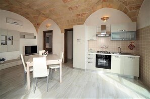 A modern kitchen with white cabinetry, a built-in oven, and a dining area with a table and chairs. - Apartment 'Kambusa - Pozzo Pasulo - A' with Sea View, Wi-Fi and Air Conditioning (Morciano di Leuca)
