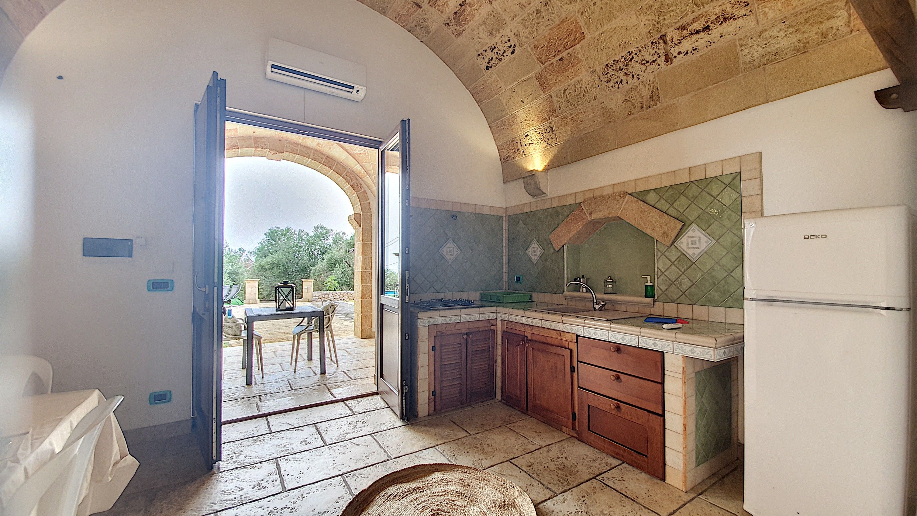 Una cocina con un arco abierto que da a un espacio exterior, un fregadero, una estufa y alacenas.