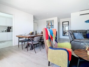 A modern living room with a sofa, a dining area with a table and chairs, and a kitchen area with cabinets and appliances. - Apartment 'Casa Cegonha, Marina Village Olhão' with Mountain View, Wi-Fi and Air Conditioning (Olhão)