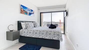 Ein modernes Schlafzimmer mit einem großen Bett, einem Nachttisch, einem blauen Teppich und Blick auf die Stadt durch ein großes Fenster.