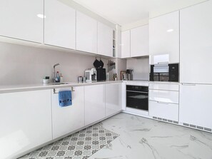 A modern kitchen with white cabinetry, a built-in oven, and a coffee machine. - Apartment 'Casa Cegonha, Marina Village Olhão' with Mountain View, Wi-Fi and Air Conditioning (Olhão)