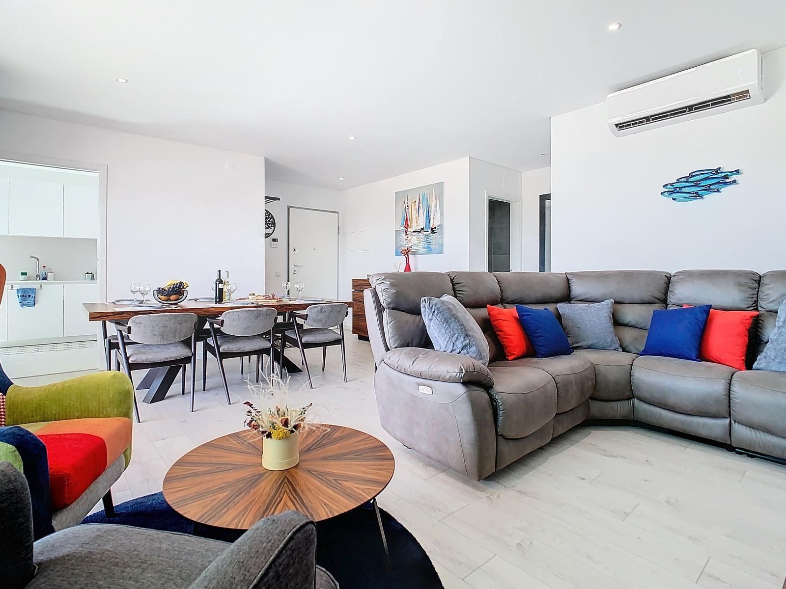 Ein modernes Wohnzimmer mit einer Eckcouch, einem Essbereich mit Tisch und Stühlen sowie einer Küchenzeile mit Schränken und Spüle.