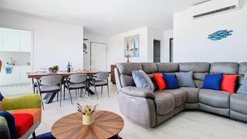 Ein modernes Wohnzimmer mit einer Eckcouch, einem Essbereich mit Tisch und Stühlen sowie einer Küchenzeile mit Schränken und Spüle.