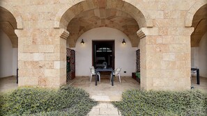 A stone archway leading to a covered patio with two chairs and a table, surrounded by low shrubs. - Apartment 'Kambusa - Pozzo Pasulo - C' with Sea View, Wi-Fi and Air Conditioning (Morciano di Leuca)