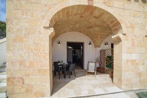 An outdoor patio area with stone walls, a table with chairs, and a decorative plant. - Apartment 'Kambusa - Pozzo Pasulo - D' with Sea View, Wi-Fi and Air Conditioning (Morciano di Leuca)