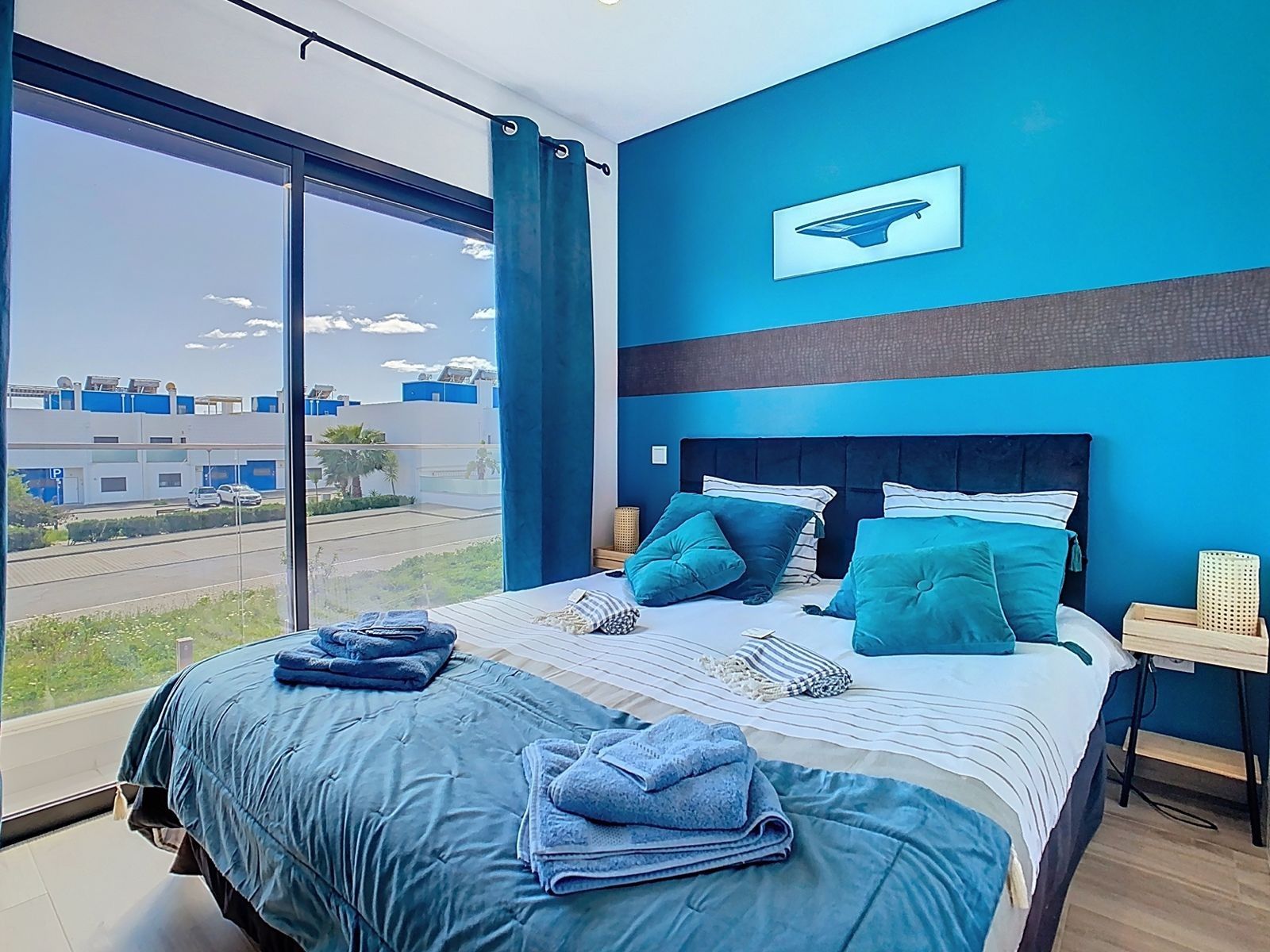 A modern bedroom with a large bed, a view of the city, and a blue accent wall.
