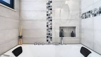 A modern bathroom with a large bathtub, a shower area, and a small shelf with toiletries.