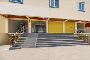 A building with a set of stairs leading to a covered entrance, a yellow shutter door, and a metal railing on the stairs.