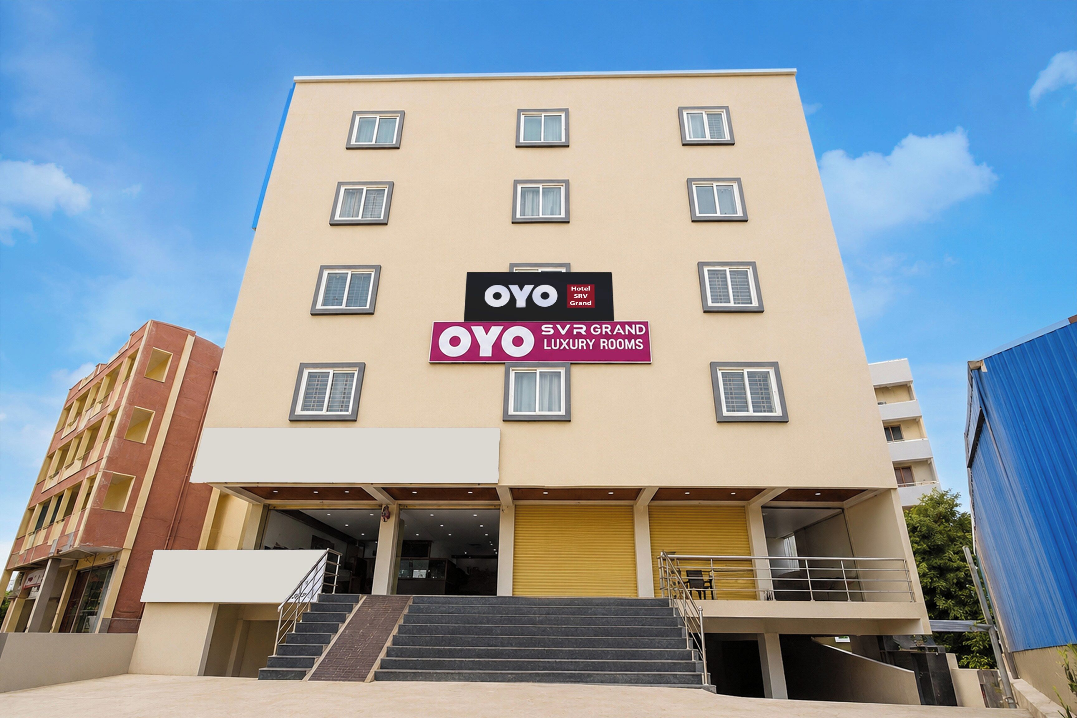 En hotelbygning med flere etager, et skilt med OYO SRV Grand og en trappe, der fører til indgangen.