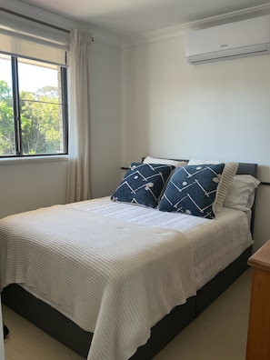 A bed with a white quilt, two pillows with a geometric pattern, a window with curtains, and a wall-mounted air conditioner. - Whisper quiet South Perth oasis near zoo, river, amenities and public transport (South Perth)