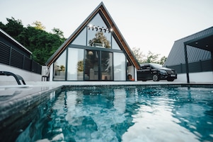 Una casa moderna con piscina, un coche y un amplio ventanal.