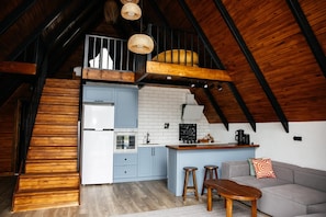 A loft-style kitchen with a wooden staircase, a dining area with a sofa and stools, and a hanging light fixture.