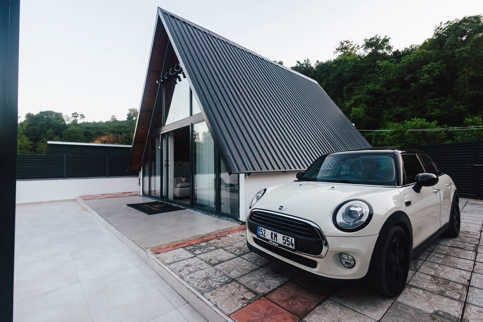 Una casa moderna con techo inclinado y un auto blanco estacionado adelante.