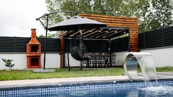 Een zwembad met een fontein, een bakoven en een overdekt zitgedeelte met stoelen en tafels.