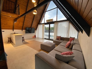 Un loft espacioso con un ventanal grande, una zona de cocina y un área de estar con sofá y reposapiés.