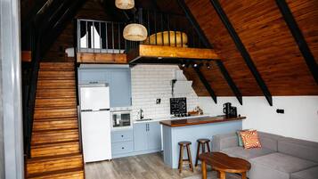 Una cocina compacta con una isla central, un comedor con taburetes y un dormitorio estilo altillo con literas.