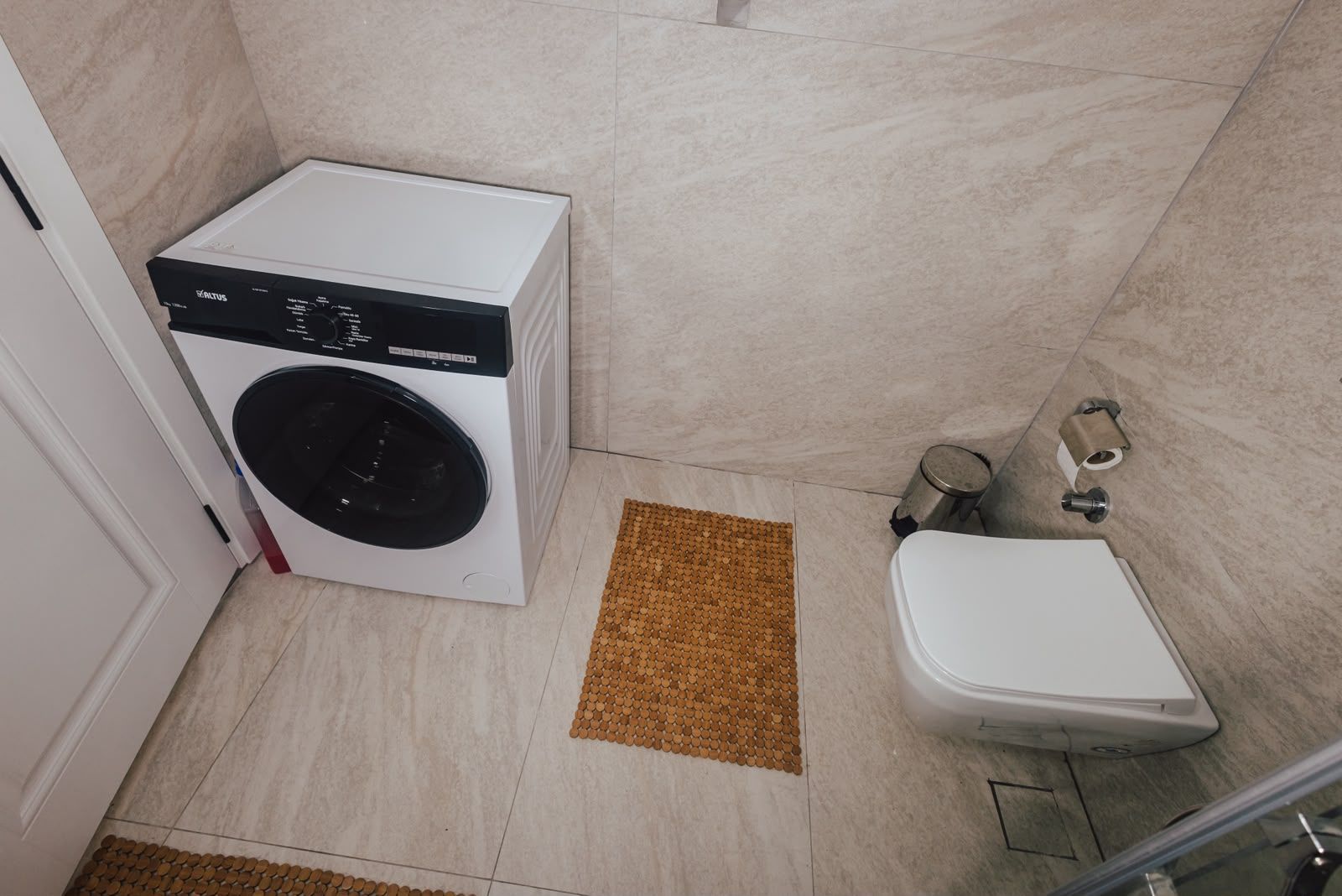Een compacte badkamer met een wasmachine, toilet en een klein afvalbakje.