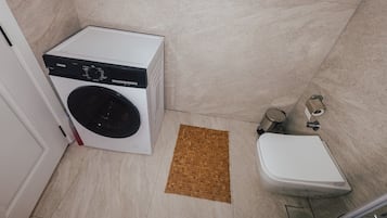 Een compacte badkamer met een wasmachine, toilet en een klein afvalbakje.