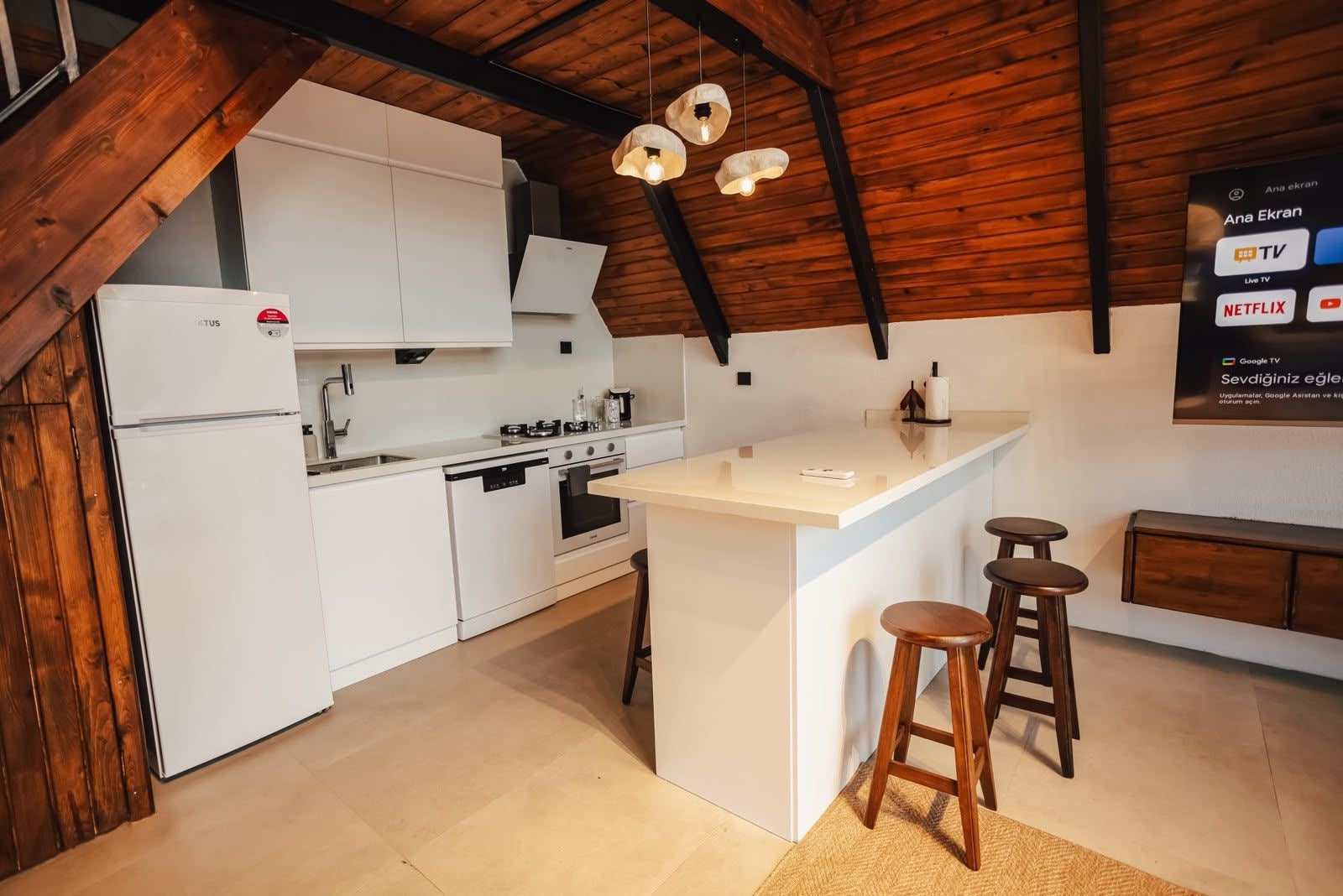 A modern kitchen with white cabinetry, a central island with stools, and a wooden ceiling.